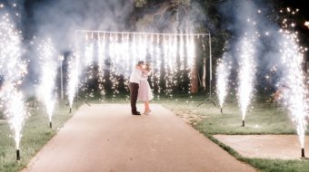 A crowd of young happy people during celebration. Sparkler in hands on a wedding - bride, groom and guests holding lights in hand. Sparkling lights of bengal fires. Wall of fountains.
